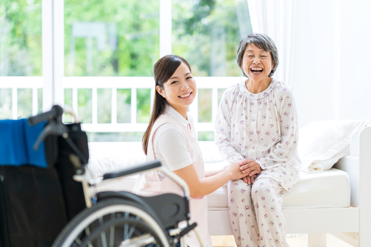 老人ホームの居室で手を取り合う高齢女性と介護スタッフの写真